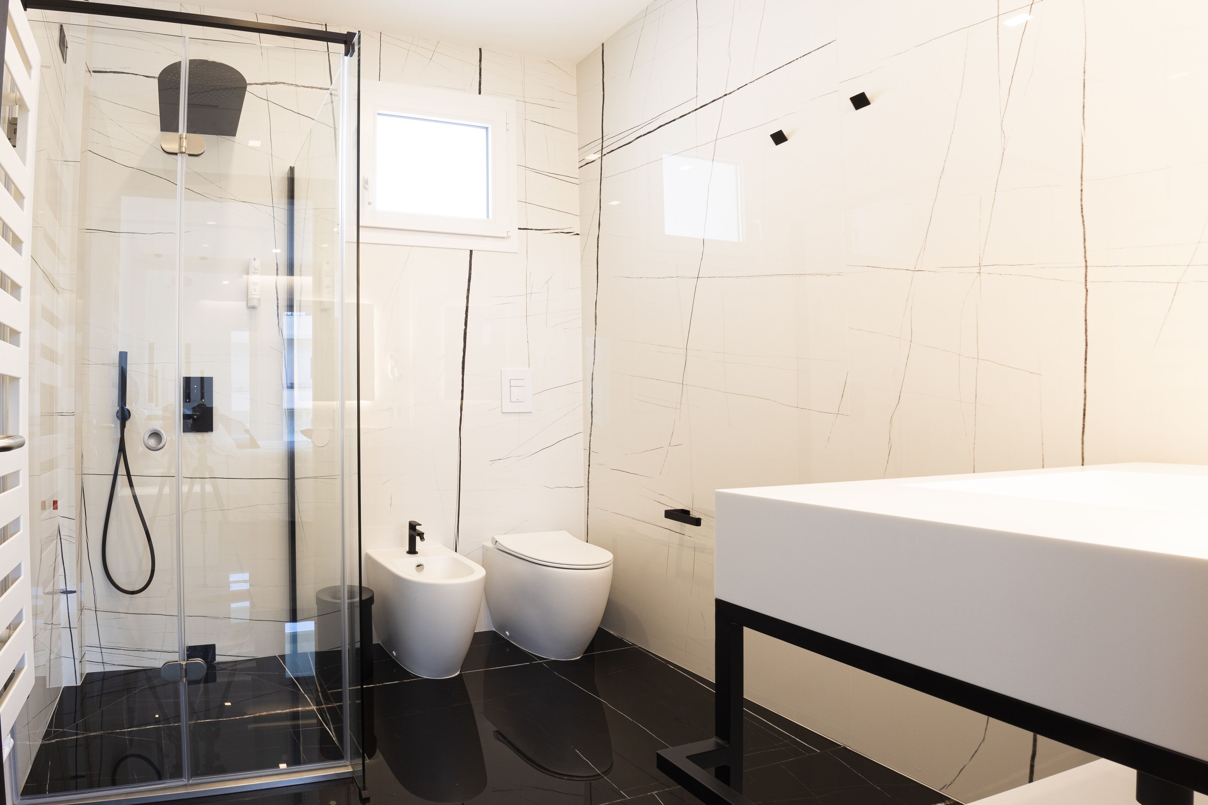 Et moderne badeværelse med en glasafskærmet brusekabine, et hvidt håndvaskarrangement og et toilet.