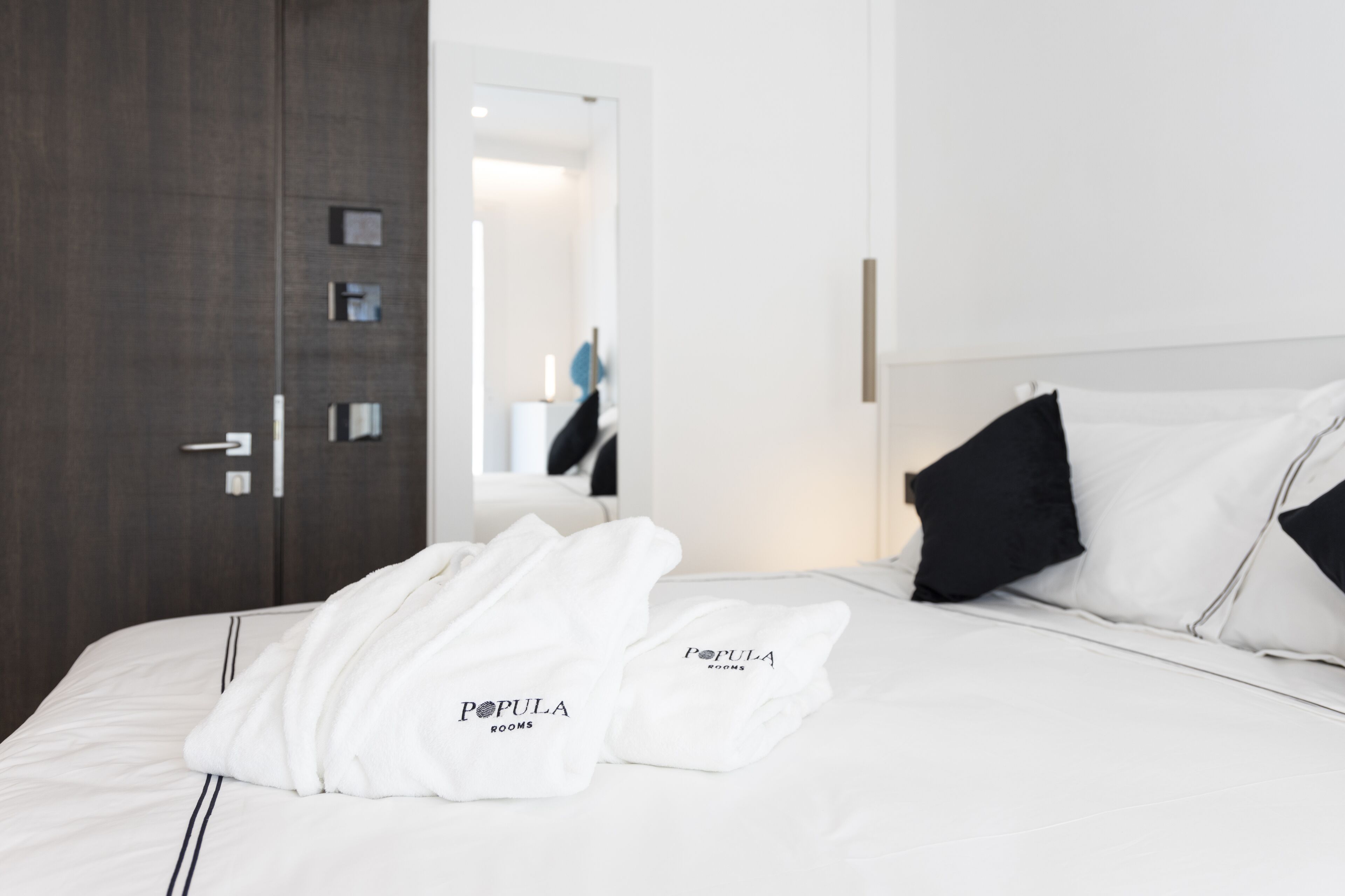 A hotel room with a neatly made bed, a large mirror, and a door with a handle.