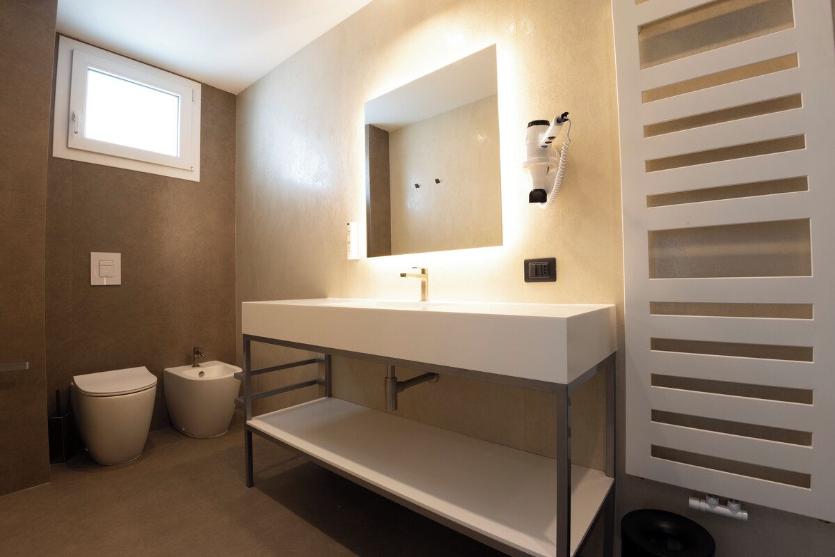 Un baño moderno con un tocador blanco, un espejo grande, un bidé y un inodoro.