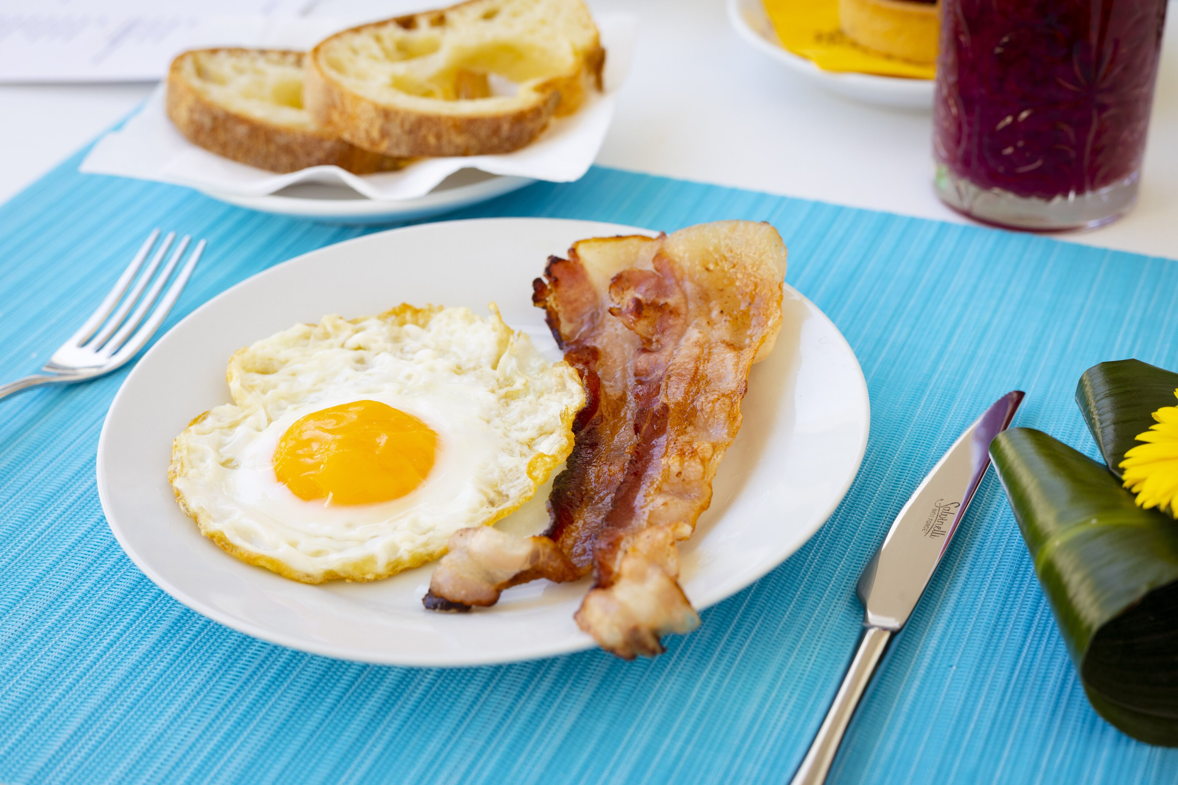 A plate with a fried egg and bacon on a white plate, placed on a blue tablecloth.