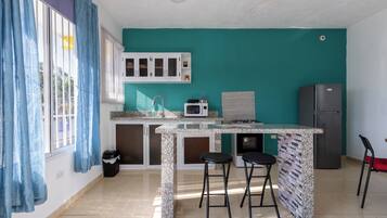 Una cocina compacta con pared verde azulada, un armario blanco, un microondas, un refrigerador y dos taburetes de bar.