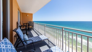 A balcony with two lounge chairs and a table, overlooking a beach with clear blue water. - 2 King bedrooms in this 15th floor condo at the Splash w/Beach Chairs! (Panama City Beach)