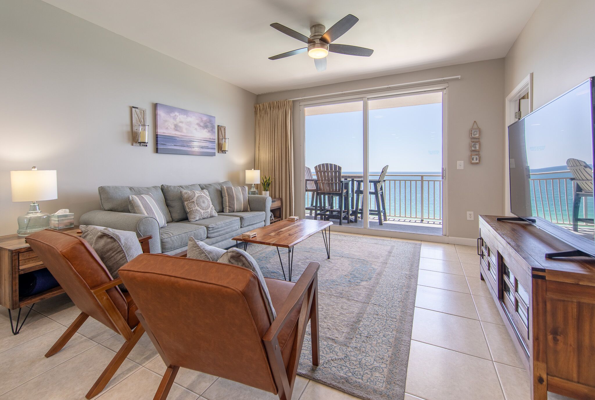 A living room with a sofa, chairs, a coffee table, a TV, and a balcony with a view.