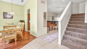 A spacious living area with a dining table and chairs, a kitchen in the background, and a staircase leading to an upper floor. - Lovely Villa with a pool/ Ideal for long stays / Message for discounts. (Davenport)