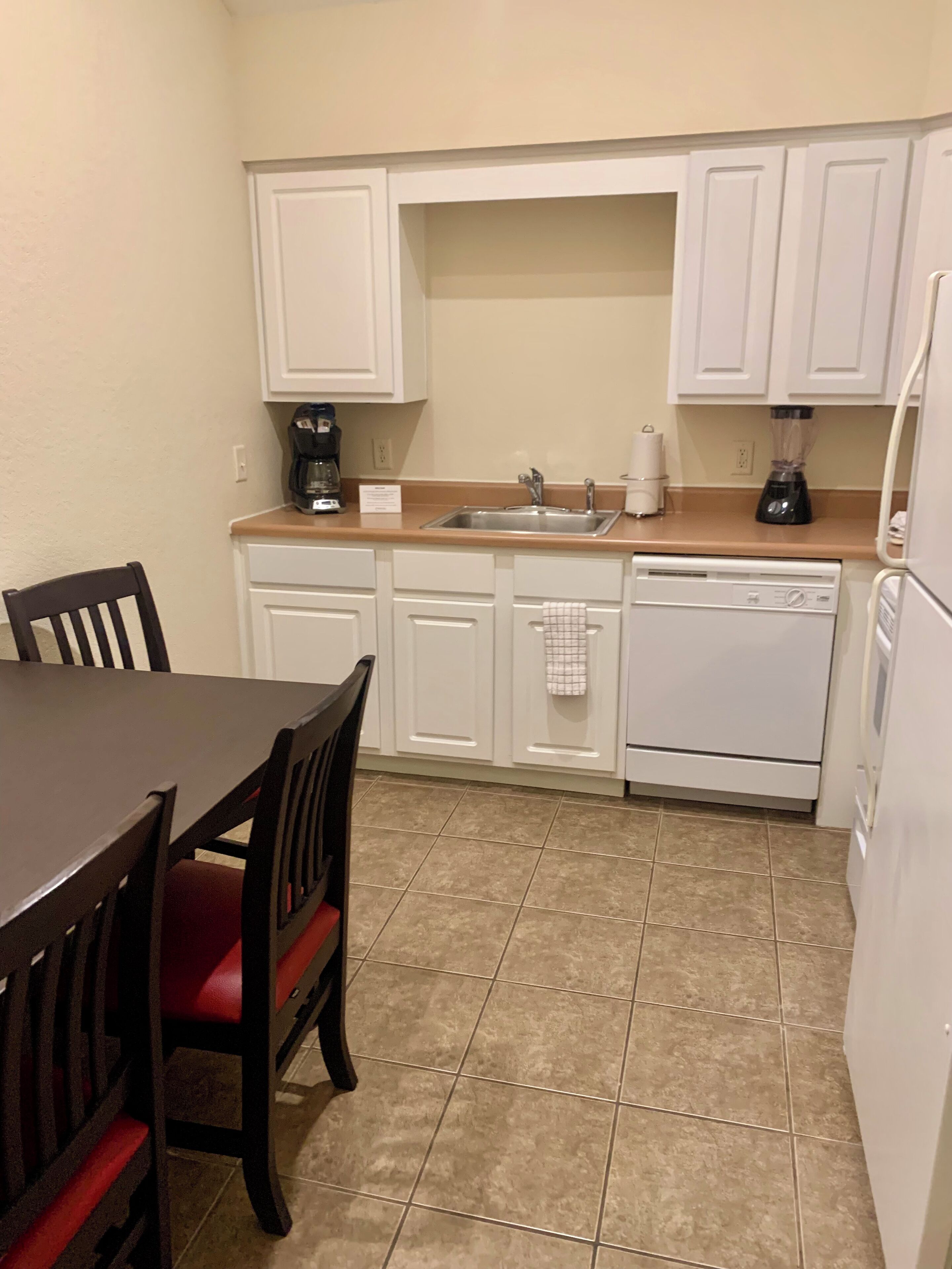 A compact kitchen with white cabinets, a sink, a coffee maker, and a dishwasher.
