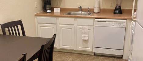 A compact kitchen with white cabinets, a sink, a coffee maker, and a dishwasher.