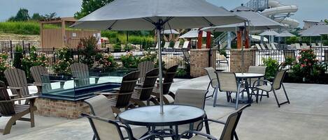 An outdoor patio area with round tables and chairs, umbrellas, and a pool in the background.