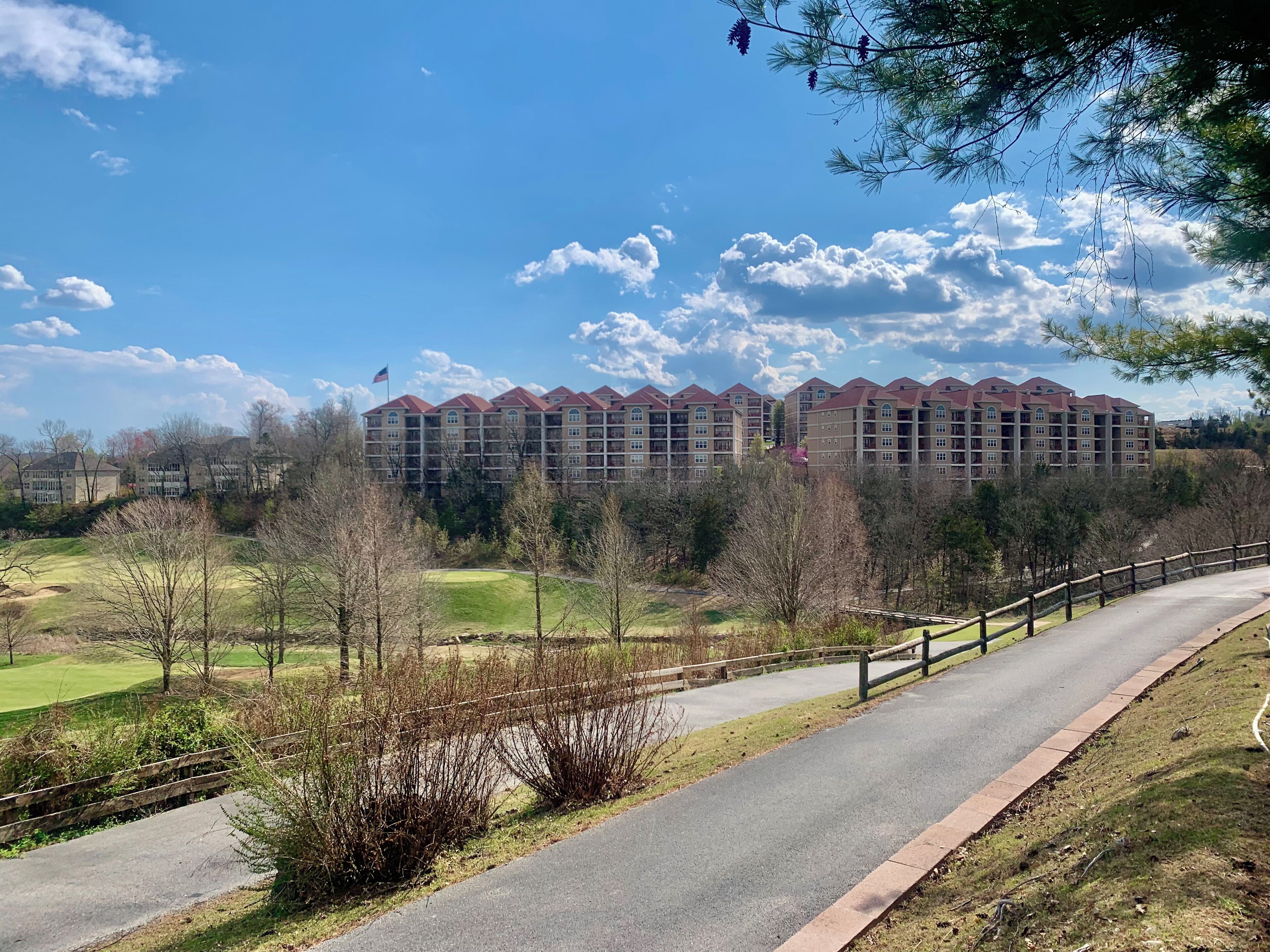 A multi-story hotel with a red roof, surrounded by a golf course and trees.