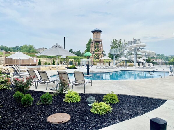 A swimming pool with lounge chairs and umbrellas, surrounded by landscaped areas and a water slide structure.
