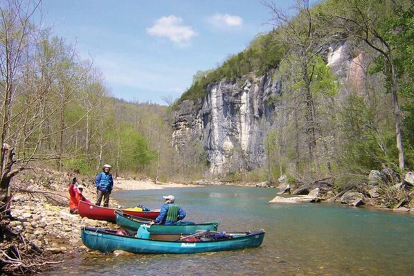 A river with canoes, a rocky cliff, and a forested area.