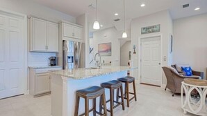 A modern kitchen with white cabinets, a marble countertop, and three wooden stools. - Tropical Paradise - Resort Style Pool - Private Elevator (Placida)