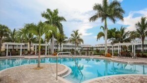 A swimming pool with palm trees and a building in the background. - Tropical Paradise - Resort Style Pool - Private Elevator (Placida)