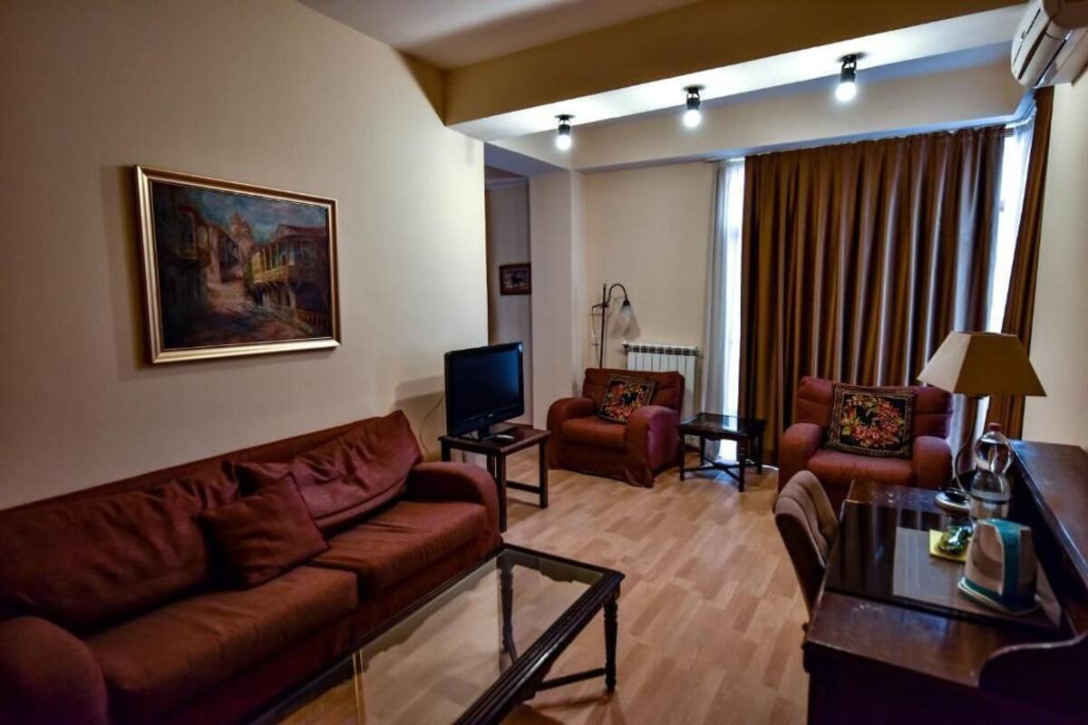 A living room with a sofa, armchairs, a coffee table, a television, and a painting on the wall.