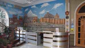 Un comptoir d’accueil orné d’une fresque représentant un paysage de montagne, avec des bâtiments en arrière-plan.