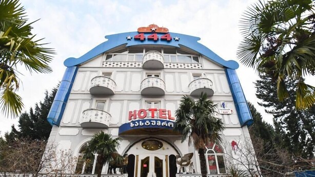 Un hôtel reconnaissable à son grand panneau « HÔTEL », à sa façade bleue et blanche et à un escalier menant à l’entrée.