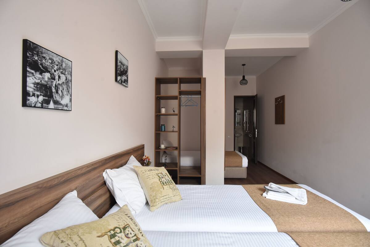 A hotel room with a bed, a wooden headboard, a wardrobe, and a bathroom visible through an open door.