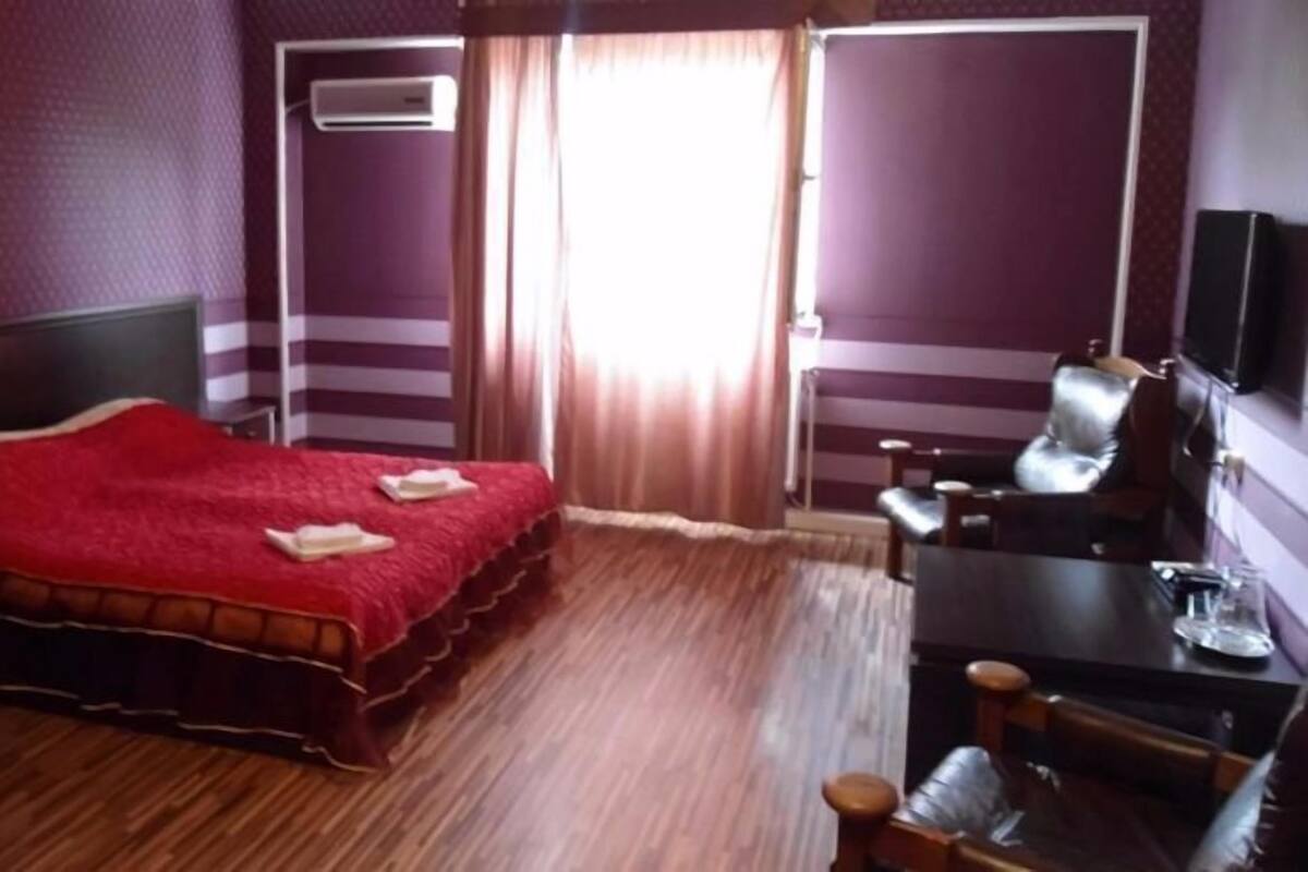 A hotel room with a bed, a desk, a chair, a television, and a window with curtains.