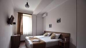 Une chambre d’hôtel avec deux lits, un bureau, une chaise, un radiateur, un climatiseur et une fenêtre avec des rideaux.