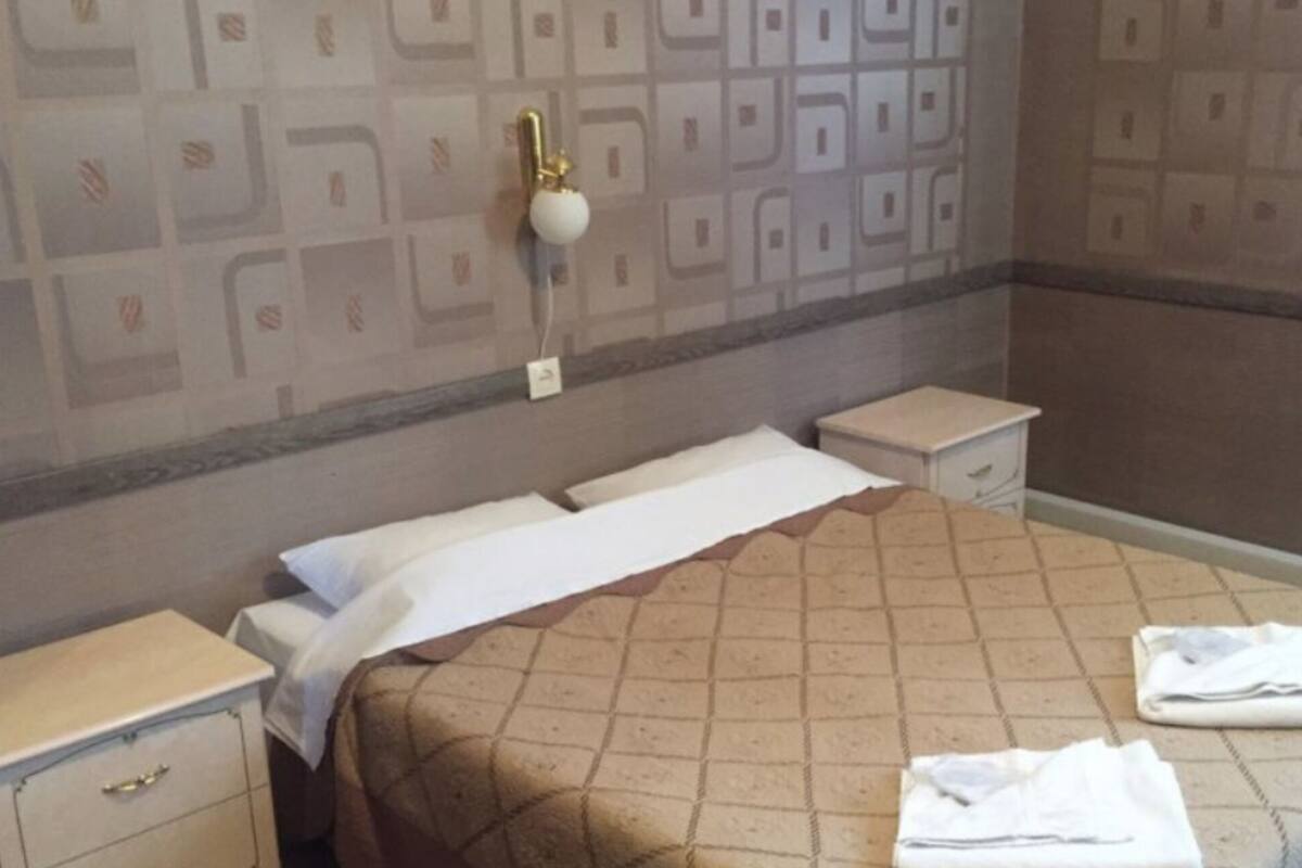 A neatly made bed with a patterned bedspread, two bedside tables, and a wall with a geometric design.