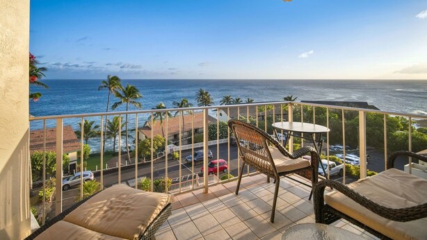 A balcony with wicker furniture, a view of the ocean, and parked cars in the background. - Captivating & Relaxing 5th Floor, Ocean Surrounds, A/C in Bedroom (Koloa)