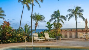 A pool area with lounge chairs, palm trees, and a view of the ocean. - Captivating & Relaxing 5th Floor, Ocean Surrounds, A/C in Bedroom (Koloa)