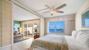A bedroom with a bed, a ceiling fan, a window with curtains, and a view of the ocean. - Captivating & Relaxing 5th Floor, Ocean Surrounds, A/C in Bedroom (Koloa)
