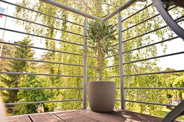 A balcony with a potted plant, metal railing, and a view of greenery.