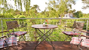 Eine Terrasse im Freien mit einem runden Tisch, zwei Holzstühlen und einer Bank mit karierten Kissen.