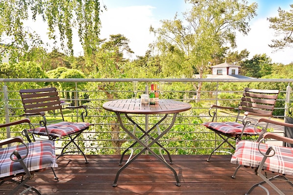 An outdoor deck with a round table, two wooden chairs, and a bench with plaid cushions.