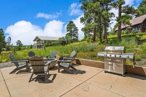 An outdoor patio with Adirondack chairs, a fire pit, and a stainless steel grill. - Large Home, Hot Tub, Close to Lakes and Shopping (Pagosa Springs)