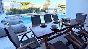 A dining area with a pool view, outdoor seating, and a table set for four.