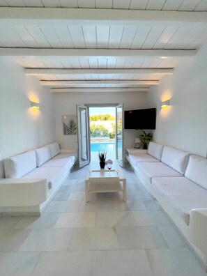 A modern living room with a pool view, white sofas, a coffee table, and a flat-screen TV.