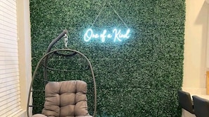 A room with a hanging chair, a neon sign reading "One of a Kind," and a green artificial grass wall.