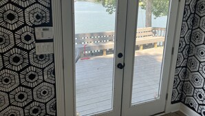 Una habitación con un papel tapiz decorado, una puerta que da a una terraza con vistas a un lago y una estructura de madera.