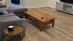 Una sala de estar con un sofá gris, una mesa de centro de madera y un televisor sobre un mueble blanco.
