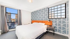 A hotel room with a large bed, a nightstand, a modern lamp, and a window with a city view.