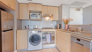 A modern kitchen with wooden cabinets, a built-in microwave, a washing machine, an oven, and a dishwasher.