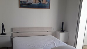 A neatly arranged bedroom with a large bed, two bedside tables, and a painting of sailboats on the wall. - Apartment small building all on port and sea 5 min beach (Noirmoutier-en-l'Île)