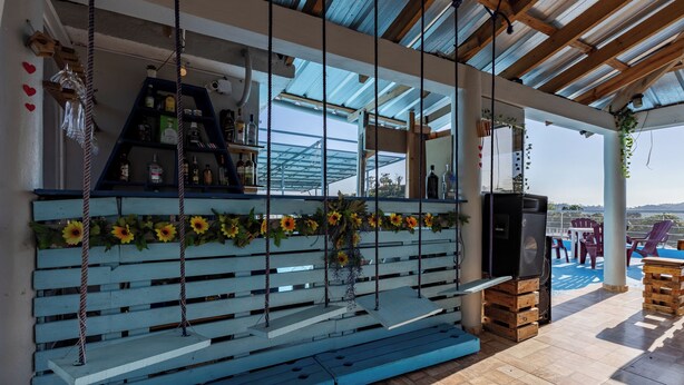 A covered outdoor seating area with a wooden bench, a grill, and a bar area with bottles and glasses. - Stylish loft in the city/ Wi-fi / Jacuzzi (Samaná)