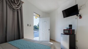 A hotel room with a bed, a television mounted on the wall, a small refrigerator, and a door leading to an outdoor area. - Stylish loft in the city/ Wi-fi / Jacuzzi (Samaná)