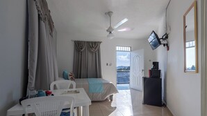A room with a bed, a desk, a chair, a ceiling fan, a TV, and a view of the sea. - Stylish loft in the city/ Wi-fi / Jacuzzi (Samaná)
