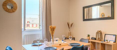 A dining area with a table set for four, a mirror on the wall, and a window with curtains.