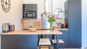 Una cocina moderna con una isla central, microondas, campana extractora de acero inoxidable y un reloj en la pared.