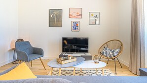 Una sala de estar moderna con un televisor de pantalla plana, un sillón gris, una silla de mimbre y una mesa de centro.