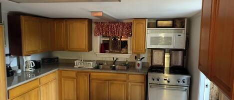A compact kitchen with wooden cabinets, a microwave, a stove, and a sink.