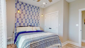 A bedroom with a patterned headboard, a bed with a blue and white bedspread, a white door, and a small white table.