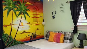 Une chambre à coucher comprenant un lit, une table de chevet, une lampe, un ventilateur de plafond, une fresque murale et une fenêtre avec des rideaux.