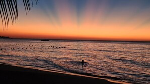 Une plage au coucher du soleil, avec une eau calme et un bateau au loin.