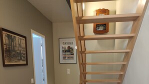 A wooden staircase with a handrail, a door at the bottom, and two framed pictures on the wall.