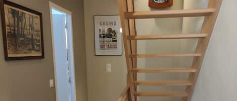 A wooden staircase with a handrail, a door at the bottom, and two framed pictures on the wall.